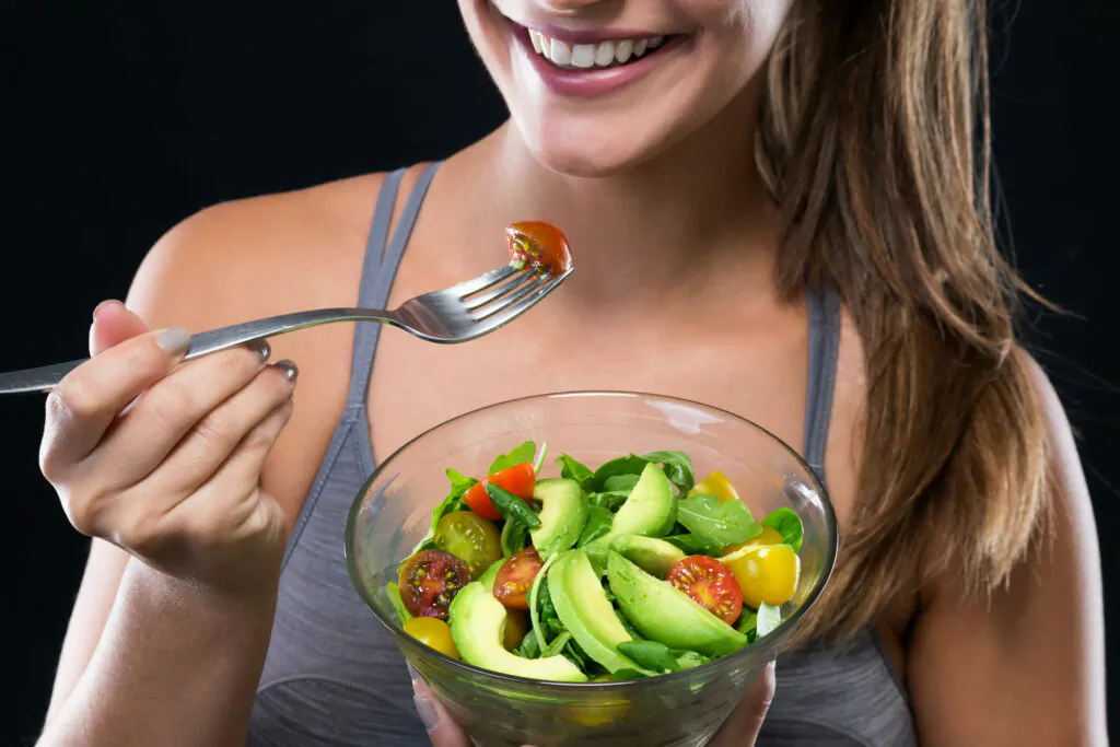 Beautiful young woman eating salad over black background