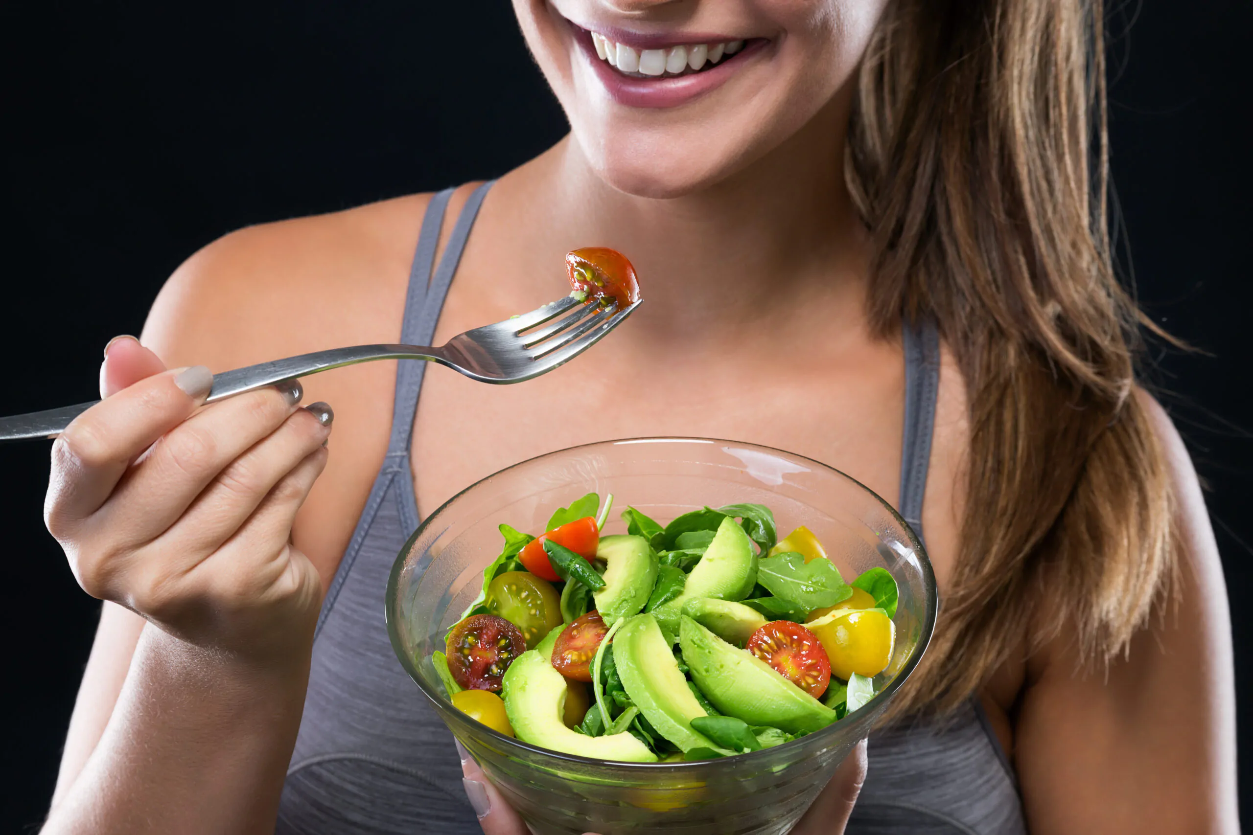 Beautiful young woman eating salad over black background